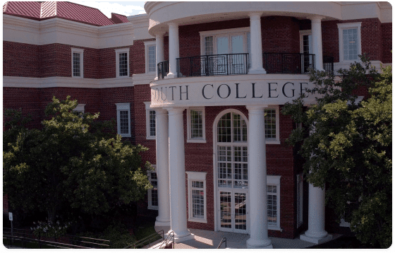 A red-brick building featuring white columns at its entrance and large windows. The building's facade displays the text "SOUTH COLLEGE" in bold, black letters. Surrounding the building are several trees and landscaped greenery.