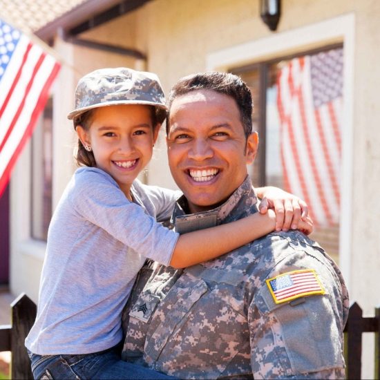 A soldier in a camouflage uniform, proud from receiving a military grant, holds and smiles with a young girl in his arms. Both are happy, with the girl wearing a matching camouflage hat.