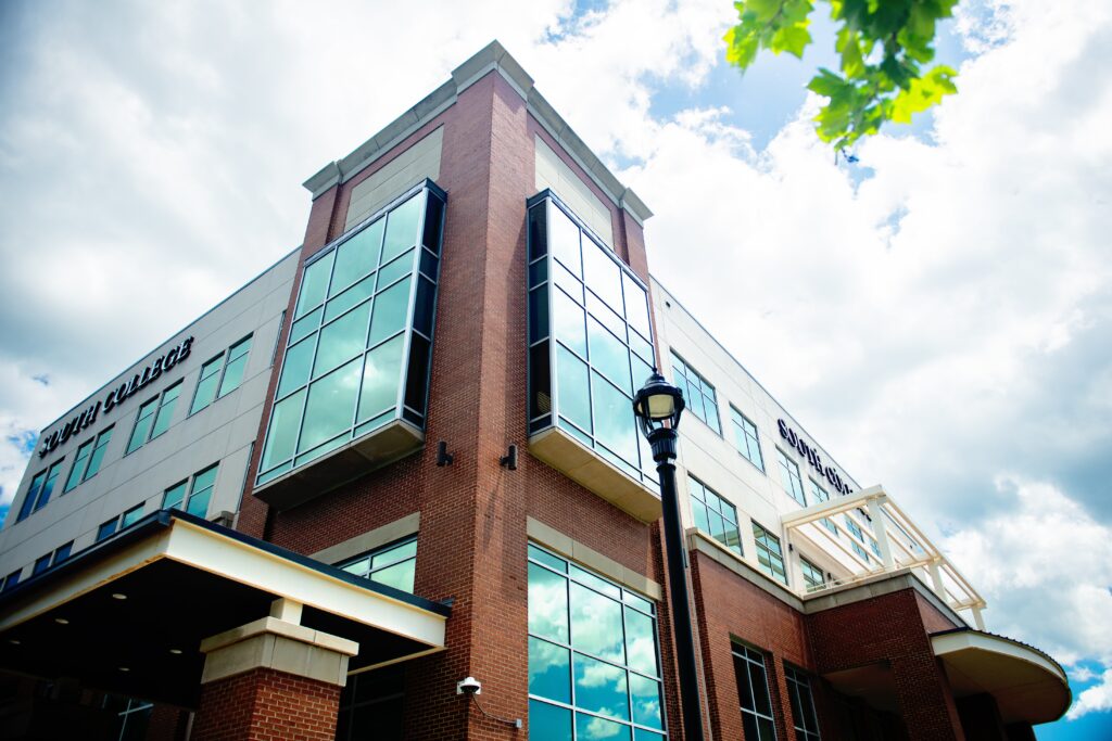 A modern brick and glass building with "South College" signage. Sunlight is reflecting off the windows.